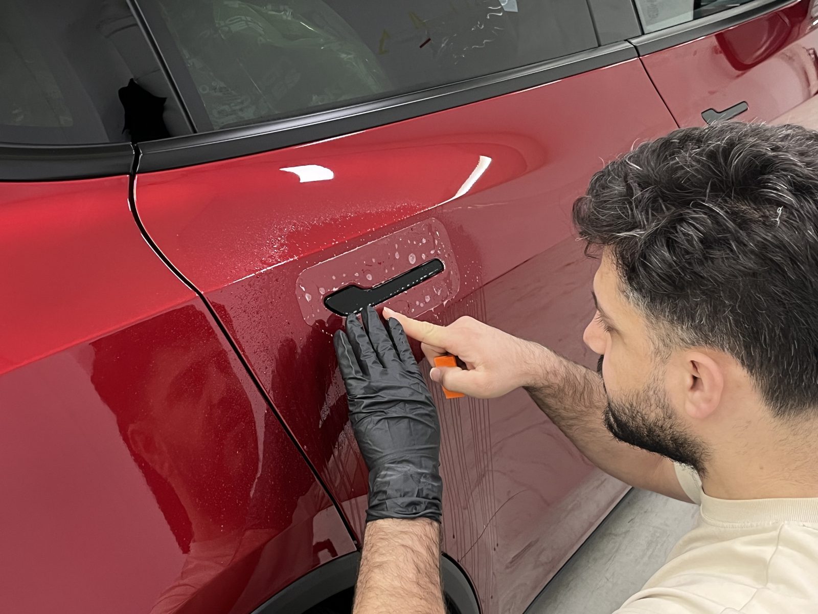 Installer applying film to a red car door panel